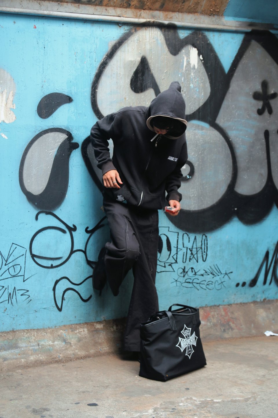 Eine Person im Kapuzenpullover lehnt an einer mit Graffiti bedeckten Wand.