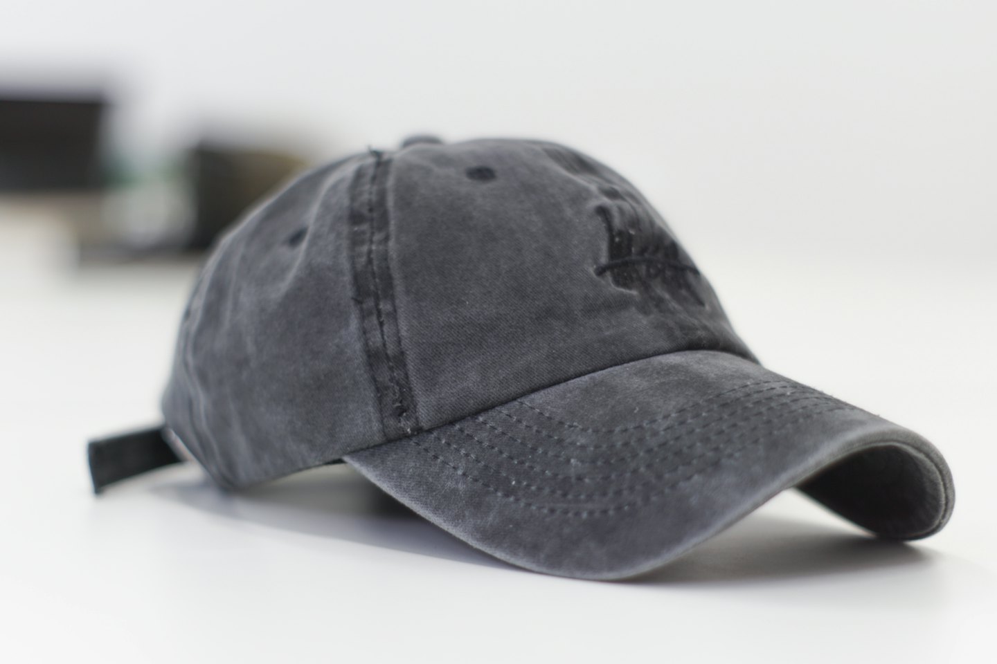 Eine schwarze Baseballkappe mit Blattmuster liegt auf einer weißen Oberfläche.