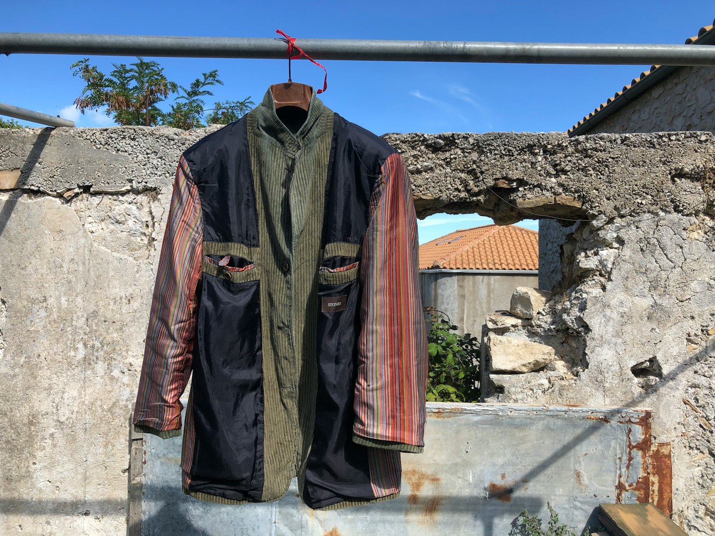 Eine Jacke aus verschiedenen Materialien hängt draußen auf einem Metallständer.